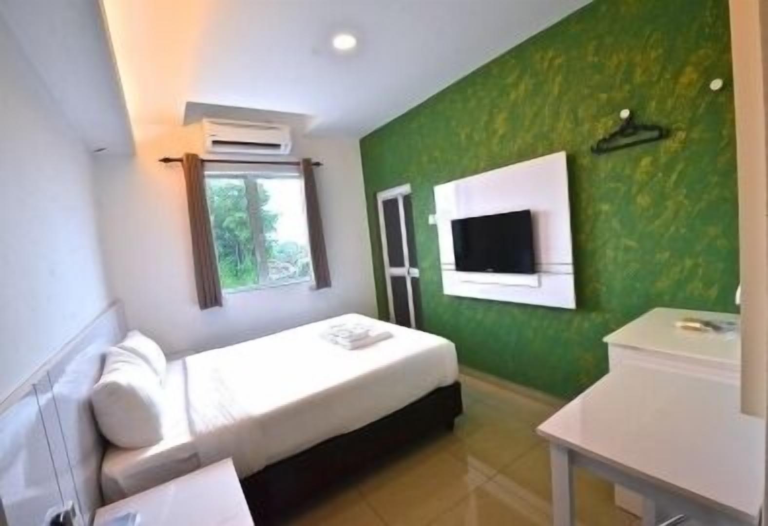 A hotel room with a bed, a TV mounted on the wall, a window with curtains, and a small table.