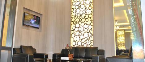 A modern lobby with a black leather sofa set, a glass coffee table, and a decorative wall with circular patterns.