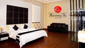 A hotel room with a large bed, a sofa, a glass table, and a wall with the hotel's logo. - Hotel Harmony In Pontianak (Pontianak)