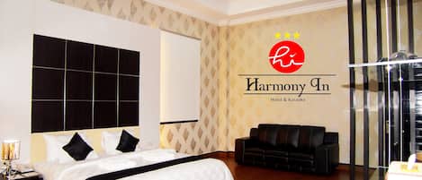 Habitación de hotel con una cama grande, un sofá, una mesa de vidrio y una pared con el logotipo del hotel.