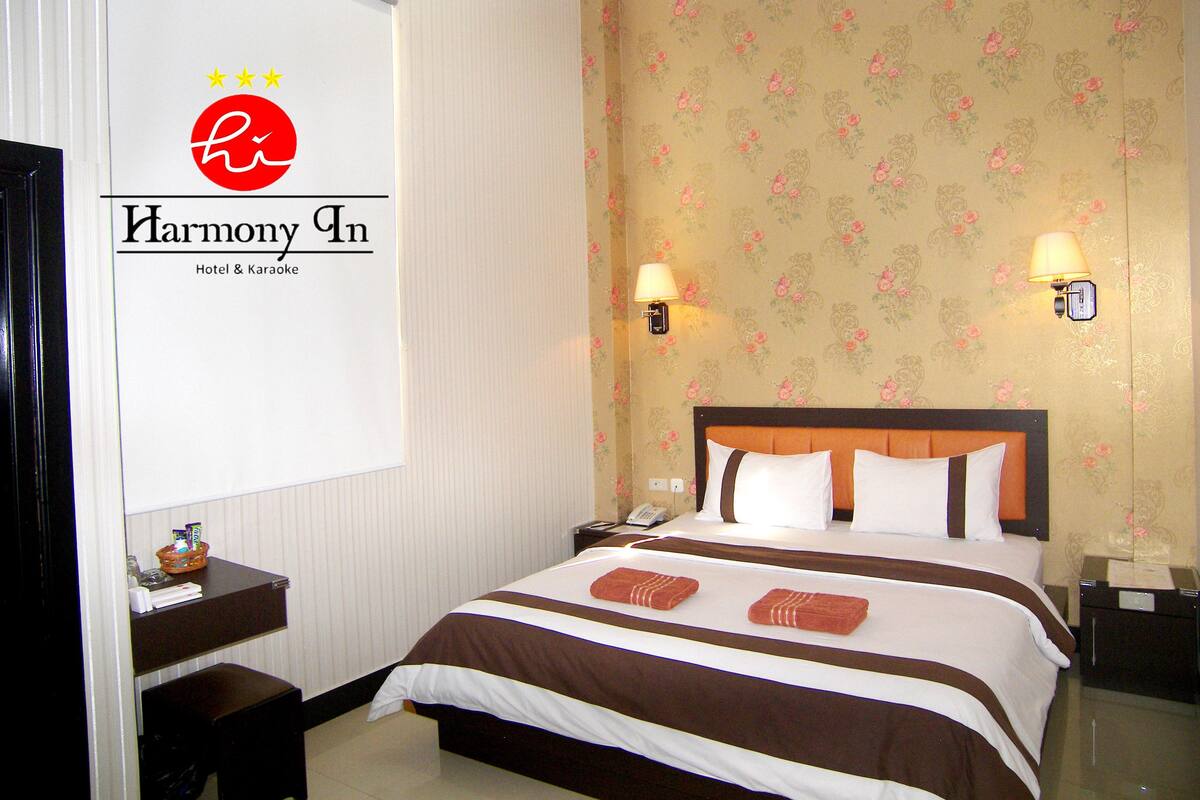 A hotel room with a bed, a nightstand, a lamp, and a wall with floral wallpaper.