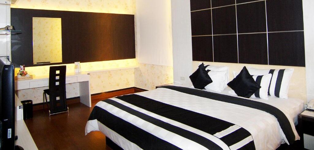 A hotel room with a large bed, a desk with a chair, a television, and a large mirror.