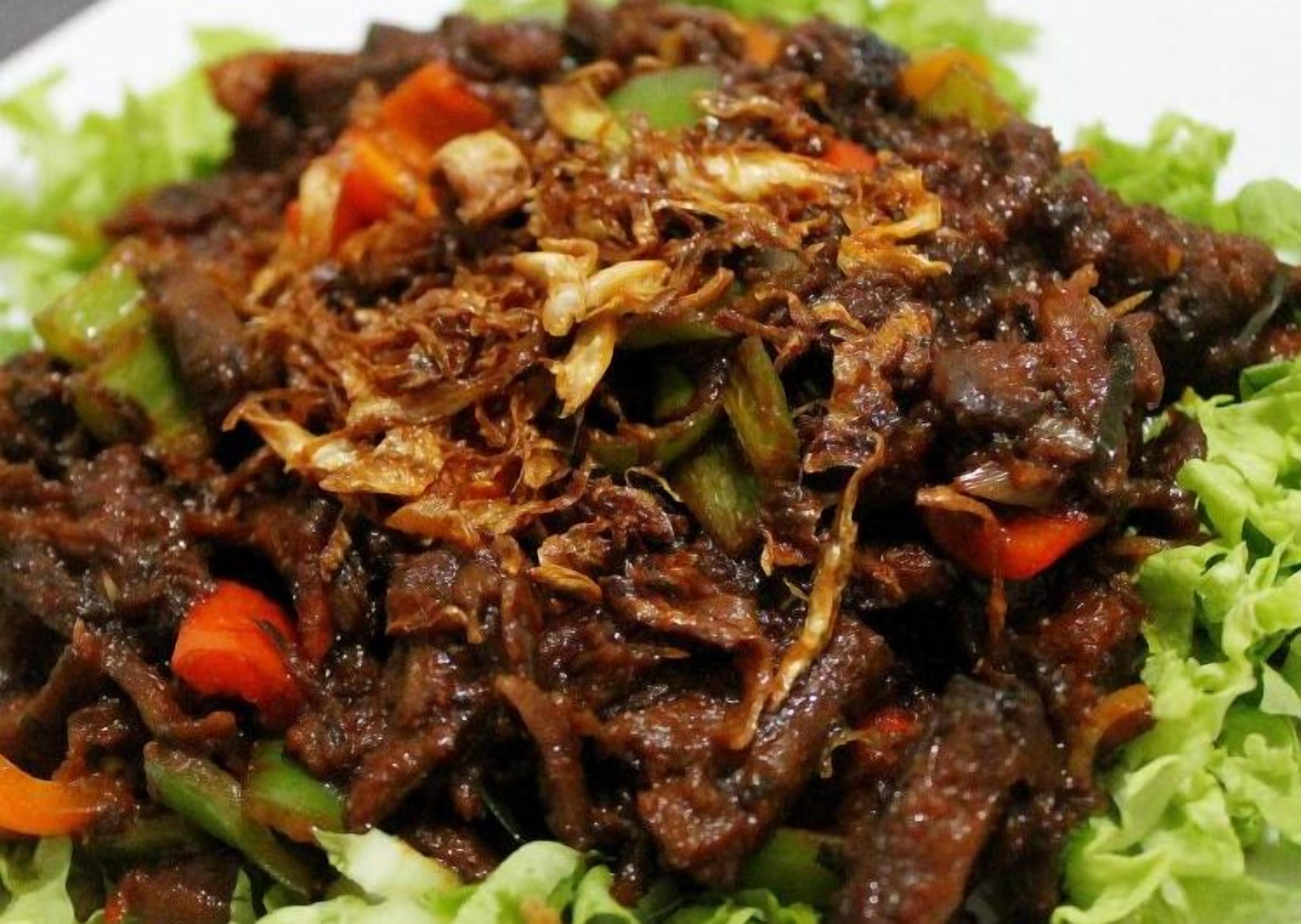 En portion wokstegt oksekød med grøntsager og stegte løg på en bund af salat.