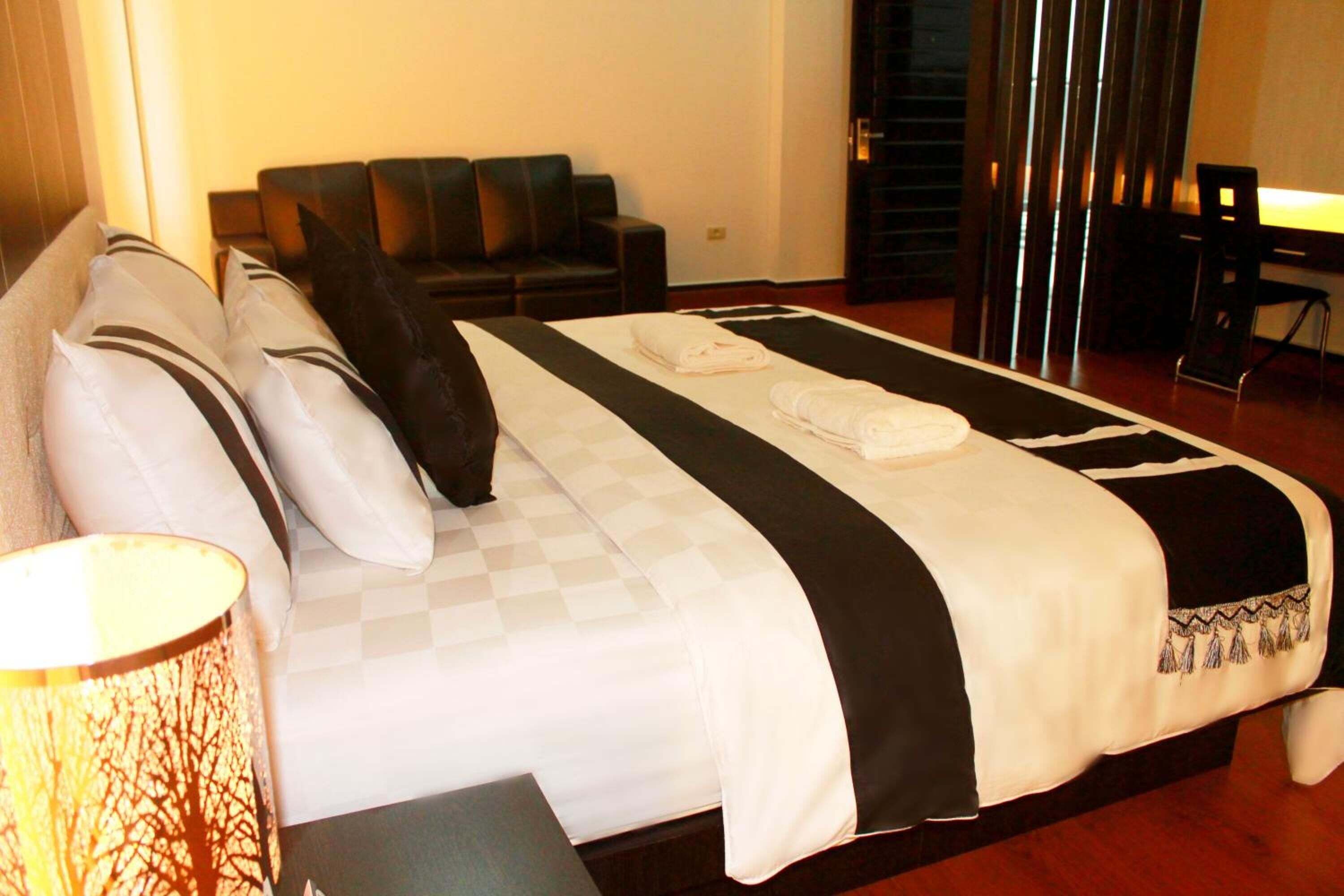 A hotel room with a large bed, a sofa, a desk, and a lamp.