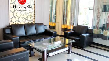 Eine moderne Lobby mit schwarzen Ledersofas, einem Glastisch und einem Schild mit der Aufschrift Harmony In Hotel & Karaoke.