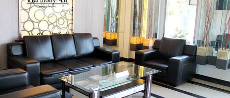 A modern lobby with black leather sofas, a glass coffee table, and a Harmony In Hotel & Karaoke sign.