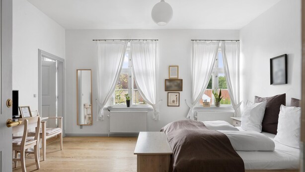 Un dormitorio con cama, escritorio, silla, ventana con cortinas y radiador.