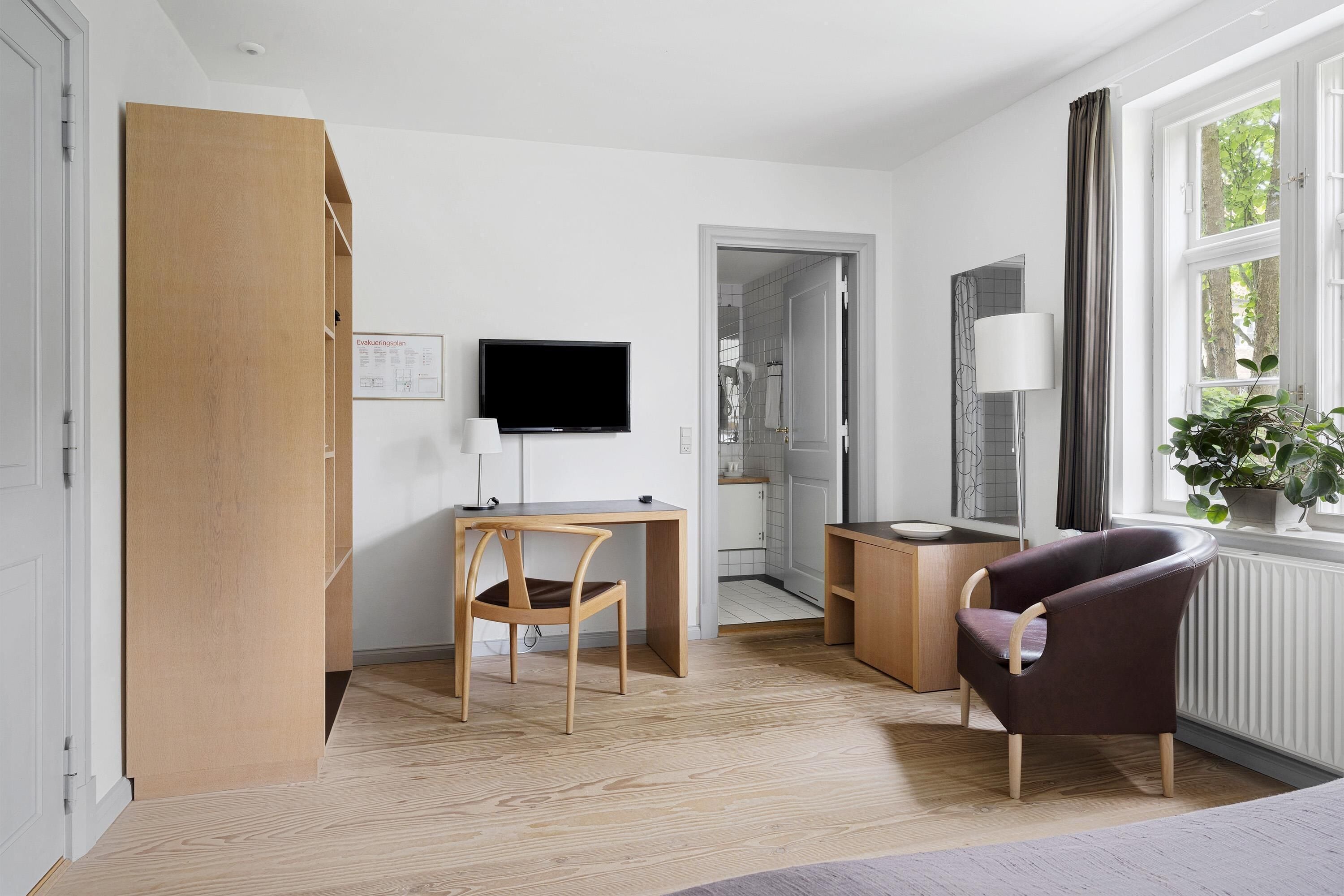 A modern room with a wooden desk, a chair, a television, a lamp, and a window with a view.