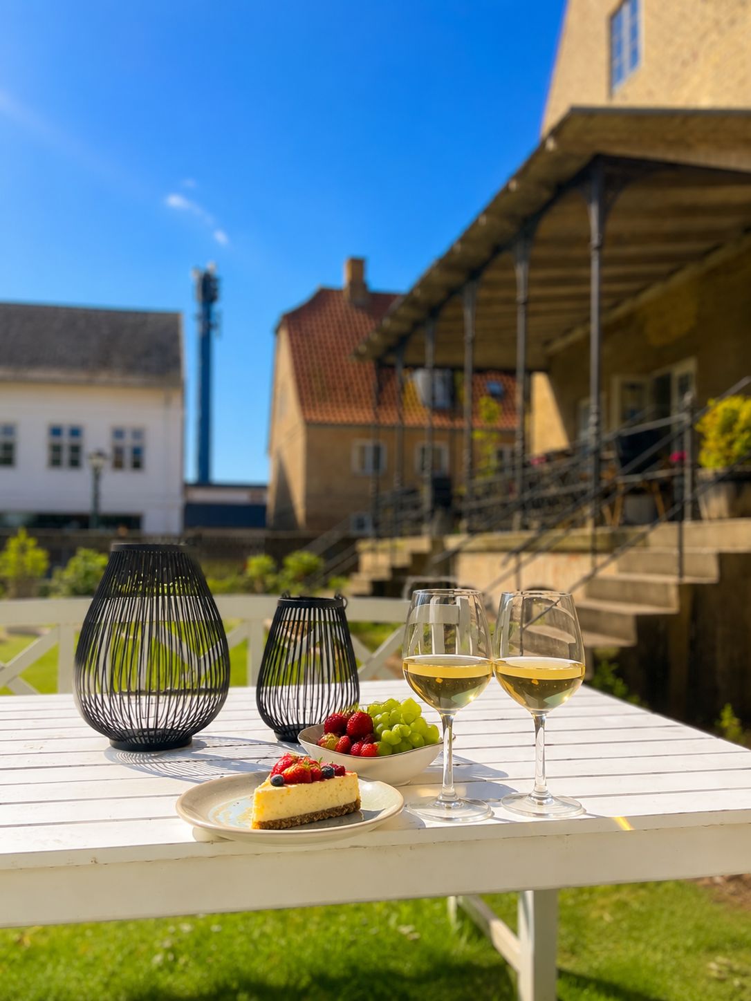 Een tafel met twee wijnglazen, een schaal fruit en een stukje cheesecake.