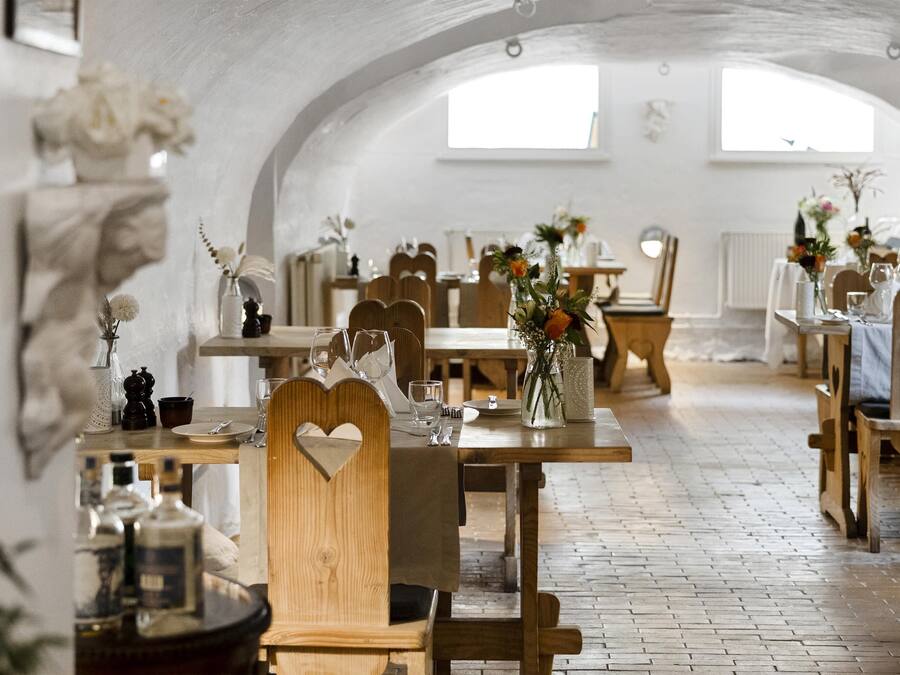 Un comedor con mesas y sillas de madera, paredes blancas y ventanas amplias.