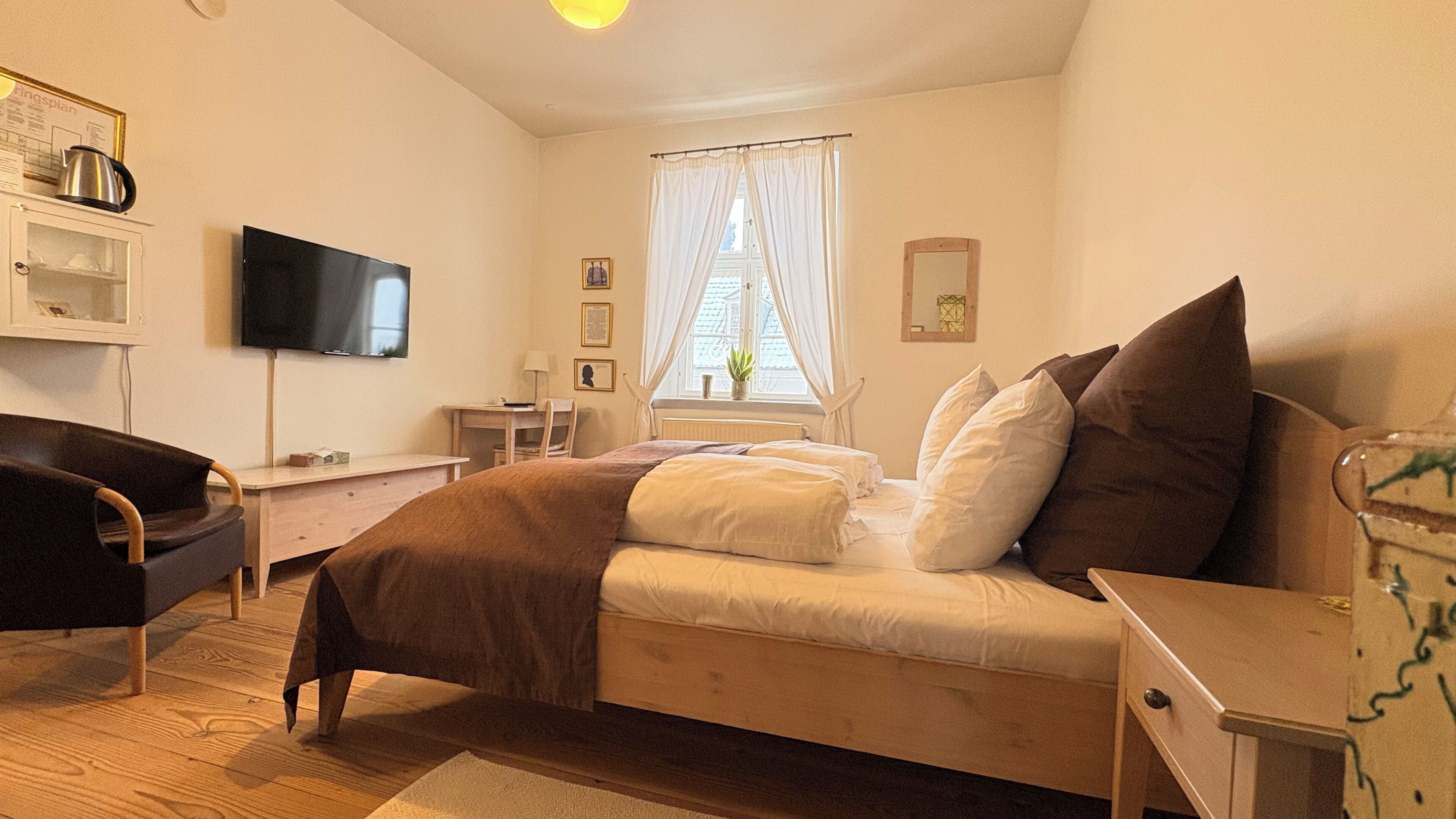 A bedroom with a bed, a desk, a chair, a television, and a window with curtains.