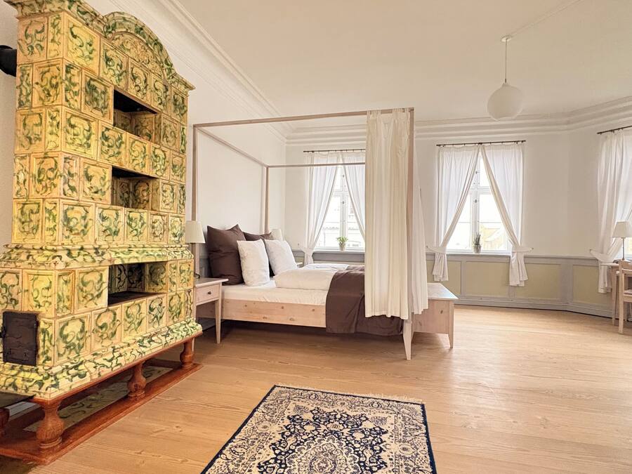 Une chambre à coucher avec un lit à baldaquin, un banc en bois, une commode à motifs et un bureau avec des chaises.
