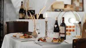Una mesa de comedor dispuesta con platos de comida, botellas de vino, copas y una vela.