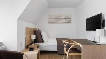 Ein modernes, kompaktes Zimmer mit Bett, Schreibtisch, Stuhl, Fernseher und einem Bild an der Wand.