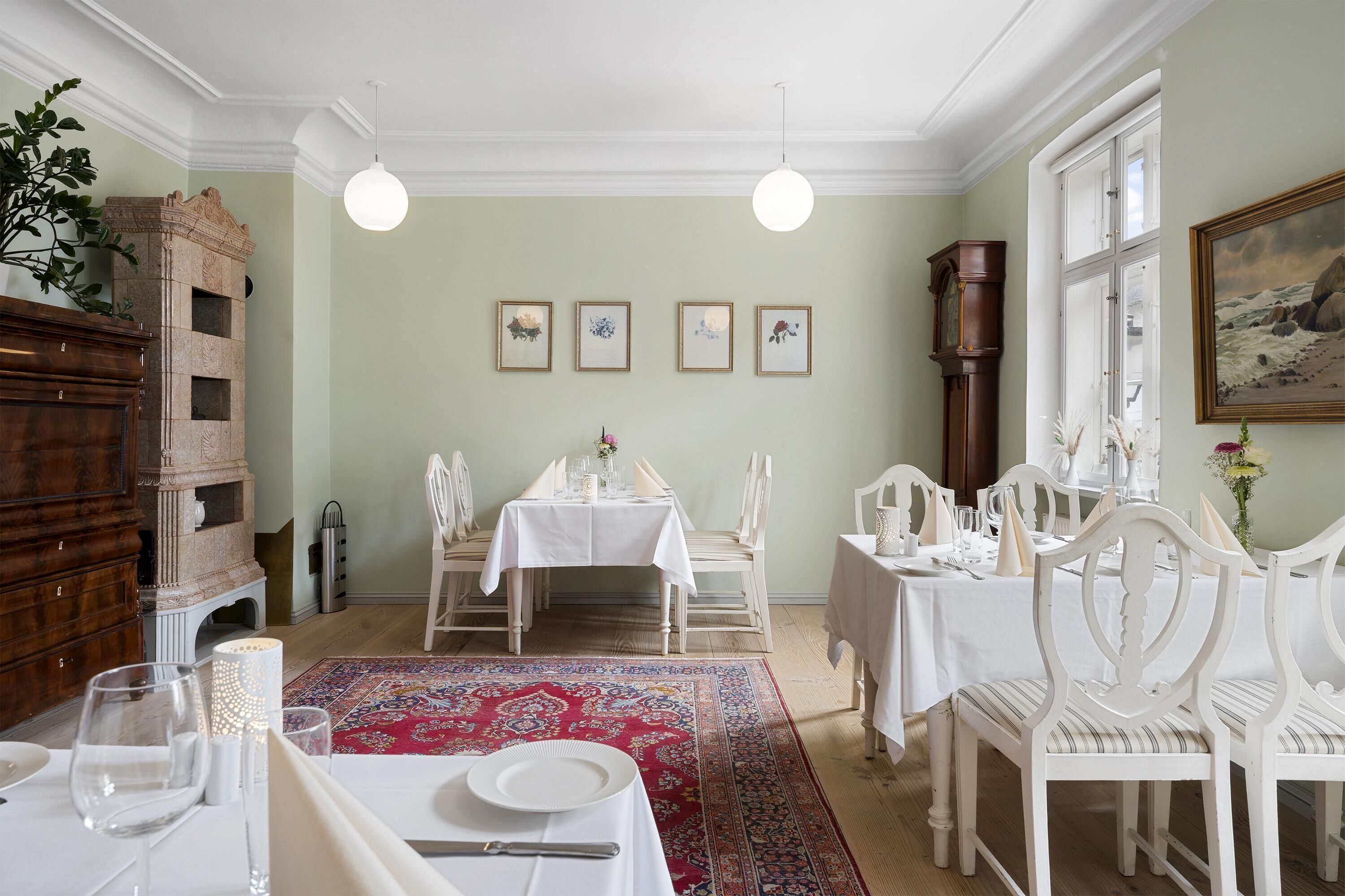 Comedor con mesas y sillas blancas, alfombra roja estampada y cuadros en la pared.