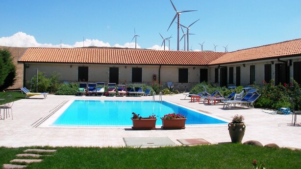 Un área de piscina con sillones de descanso y un edificio con techo de tejas.