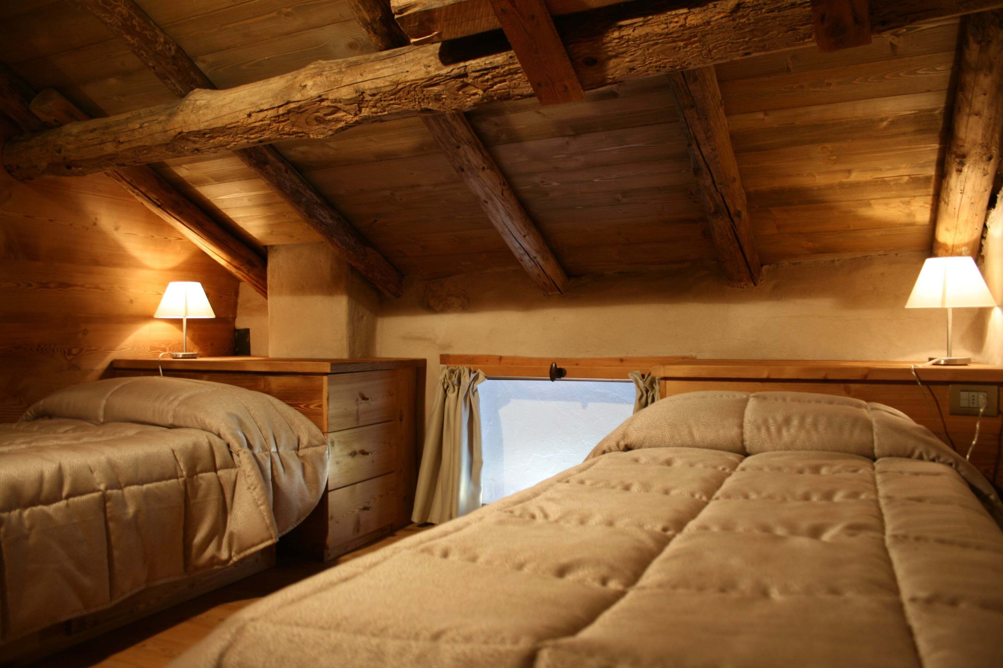 Ein gemütliches Zimmer mit zwei Betten, Holzbalken an der Decke und einem Fenster mit Vorhängen.