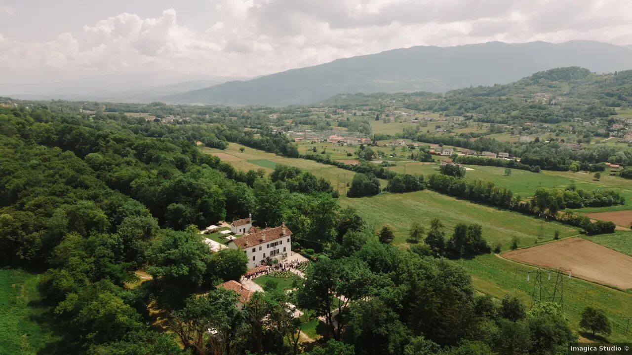 A rural landscape with a large estate featuring a prominent white building surrounded by lush greenery and fields.