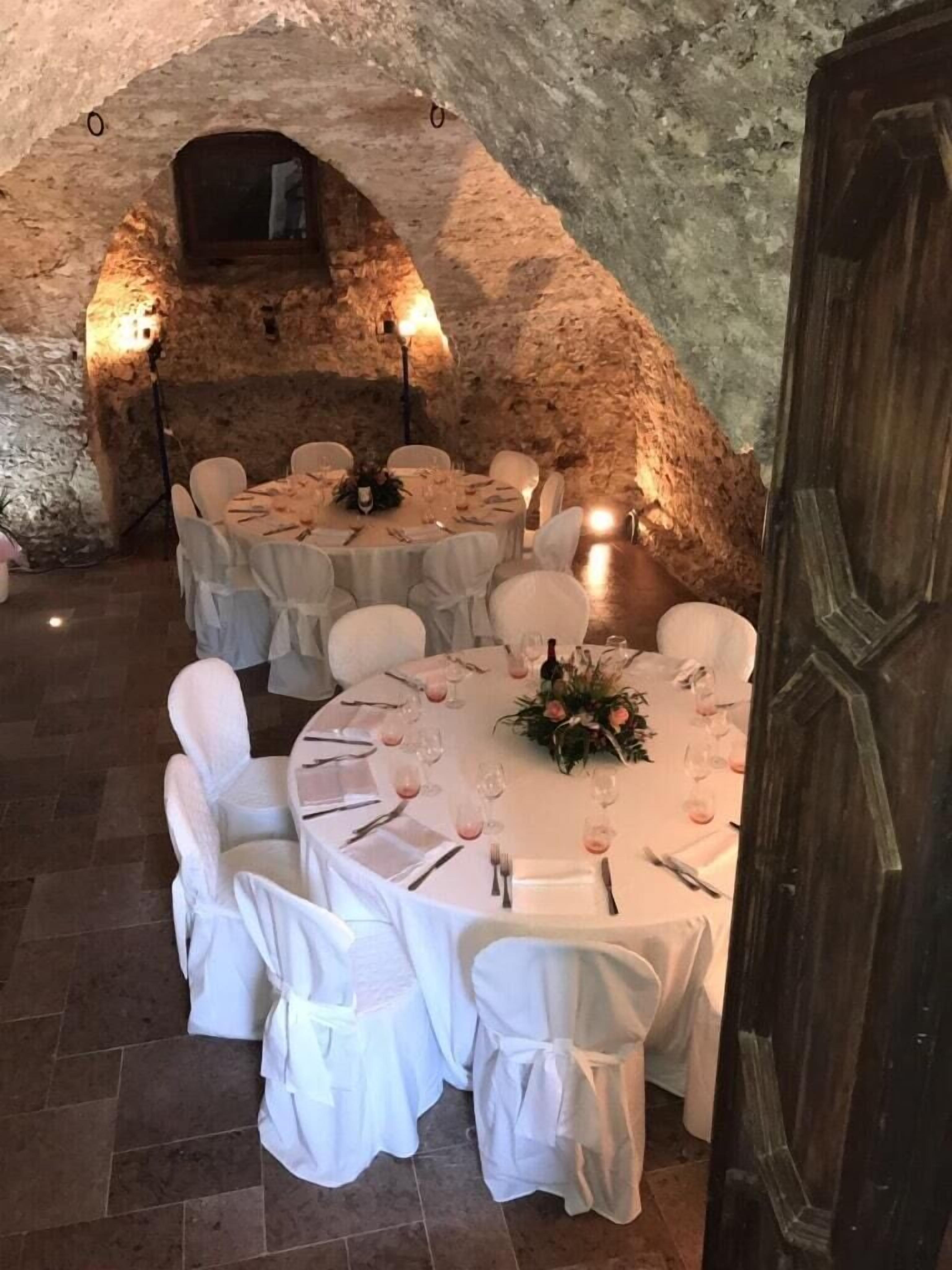 Ein Essbereich mit runden Tischen, weißen Stühlen und einer rustikalen Steinwand im Hintergrund.