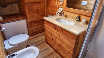 Une salle de bain rustique, située dans une cabane en bois, comprenant des toilettes, un lavabo et des meubles en bois.