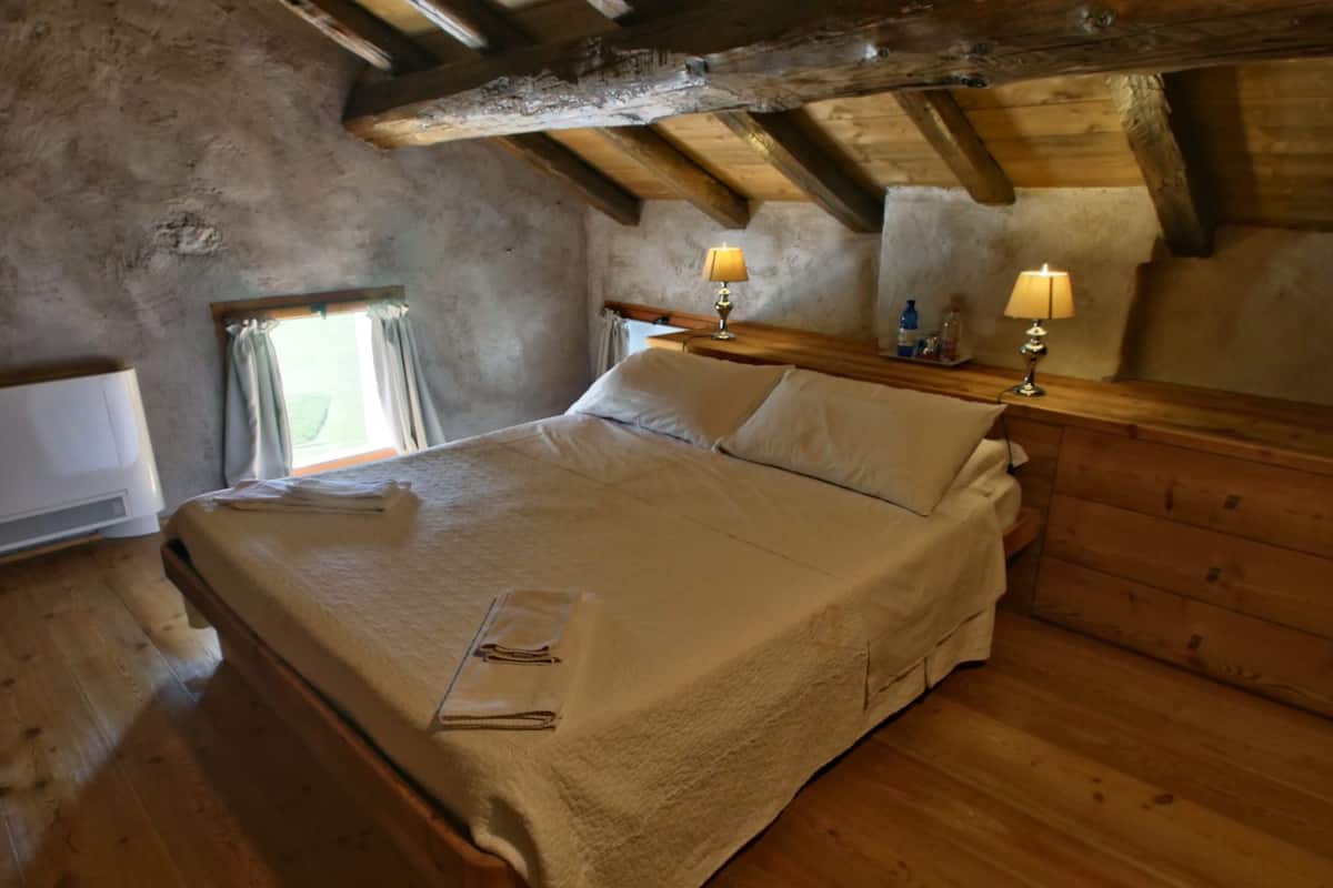 A cozy bedroom with a wooden bed, two bedside lamps, and a window with curtains.