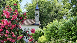 A pathway leading to a white building with a bell tower, surrounded by lush greenery and flowering plants. - Villa San Liberale - Suites & Wellness - Villa Veneta (Feltre)