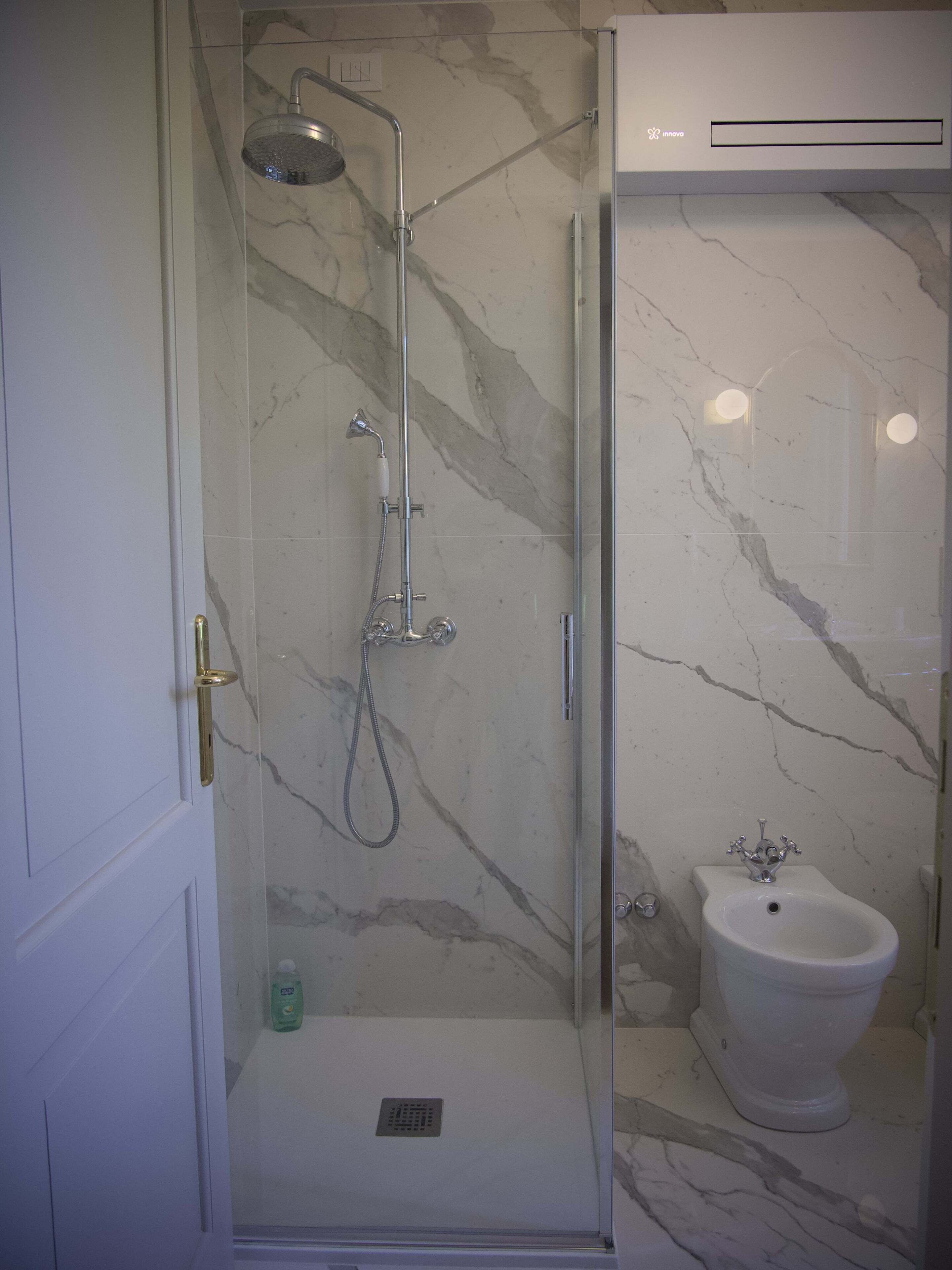 A bathroom with a glass-enclosed shower, a white pedestal sink, and marble walls.