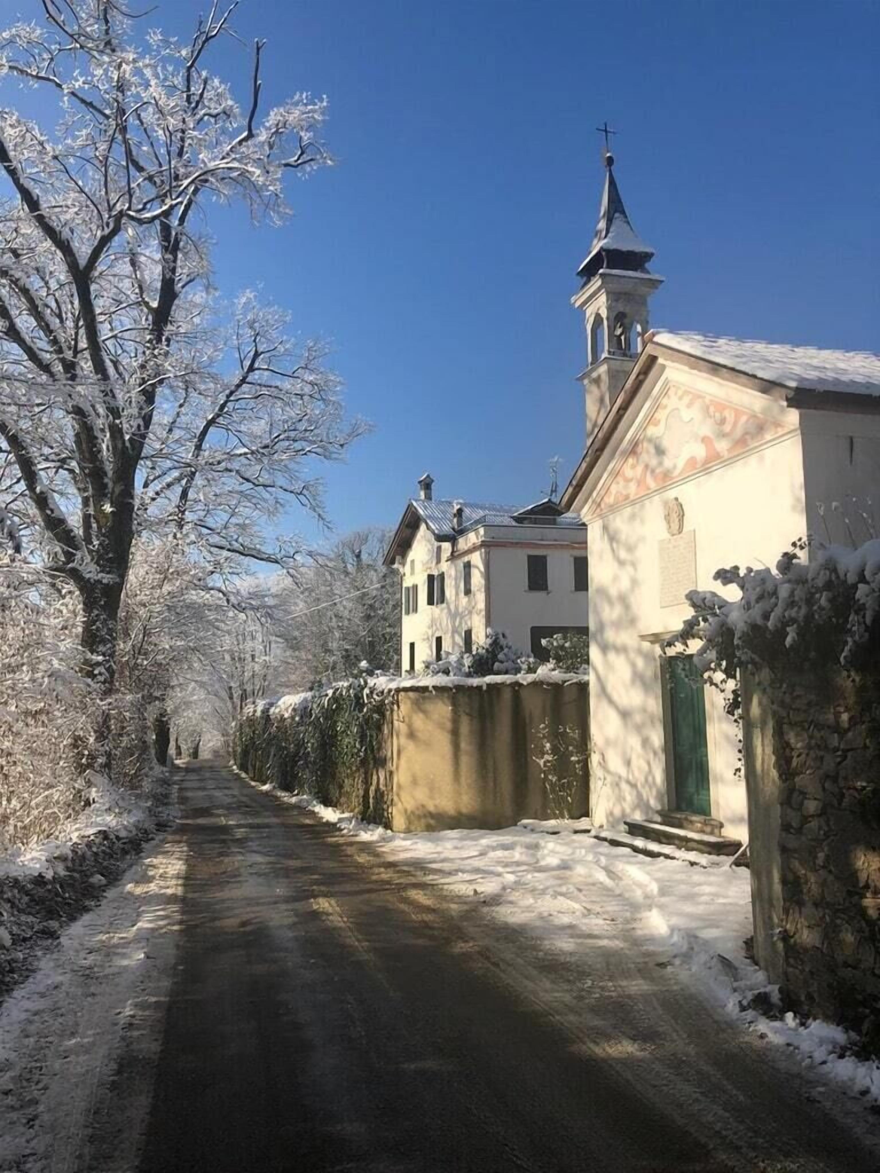 A snow-covered road leading to a church with a bell tower.