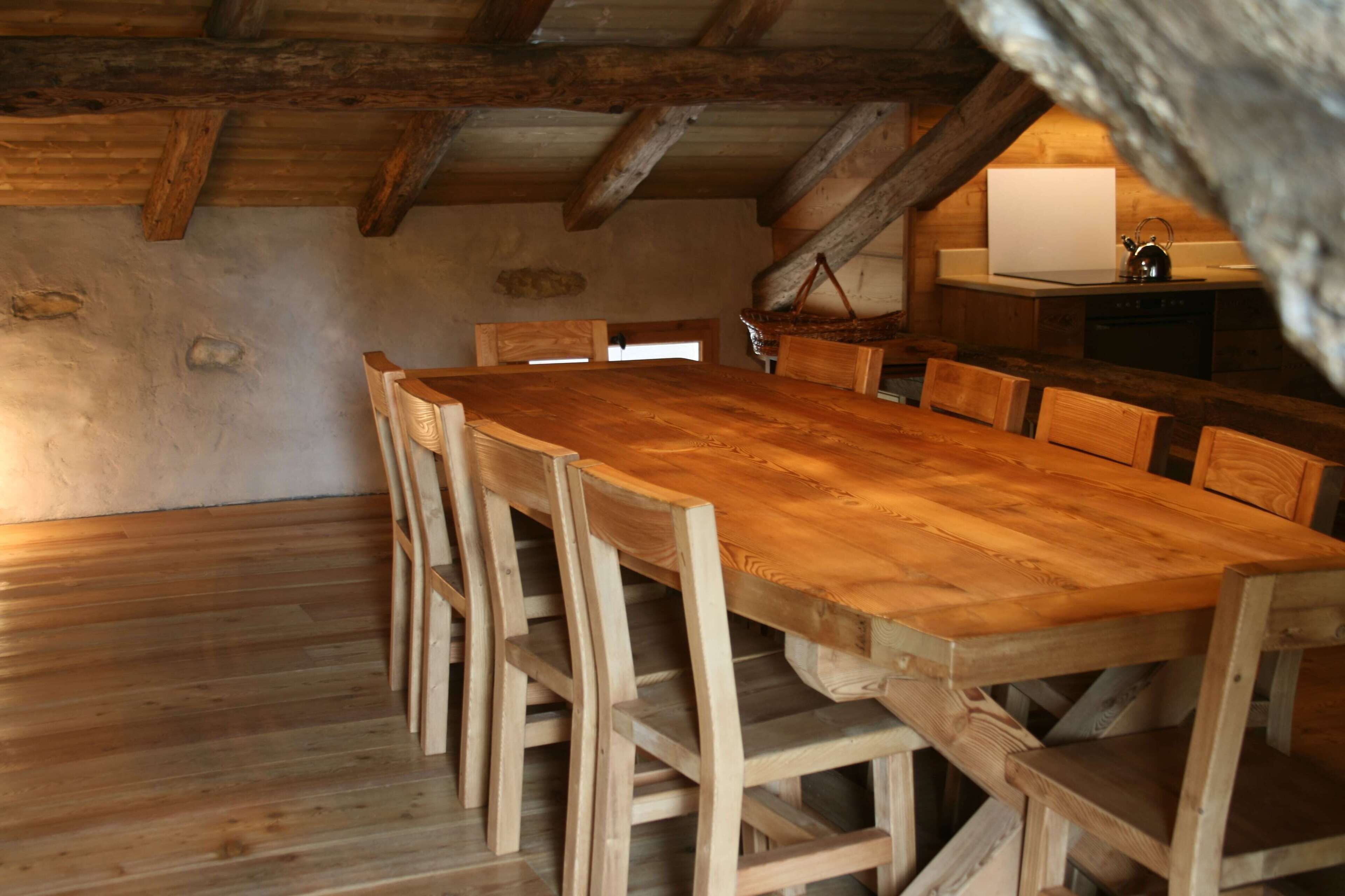 Een rustieke houten eettafel met stoelen, een houten vloer en een keukenhoek met een spoelbak en fornuis.