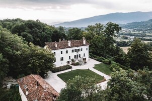 Un edificio blanco grande con fachada simétrica, rodeado de abundante vegetación y un césped bien cuidado.