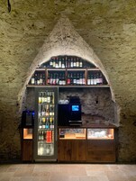 Un bar con techo abovedado de piedra, estantes llenos de bebidas embotelladas, un televisor y una vitrina refrigerada.