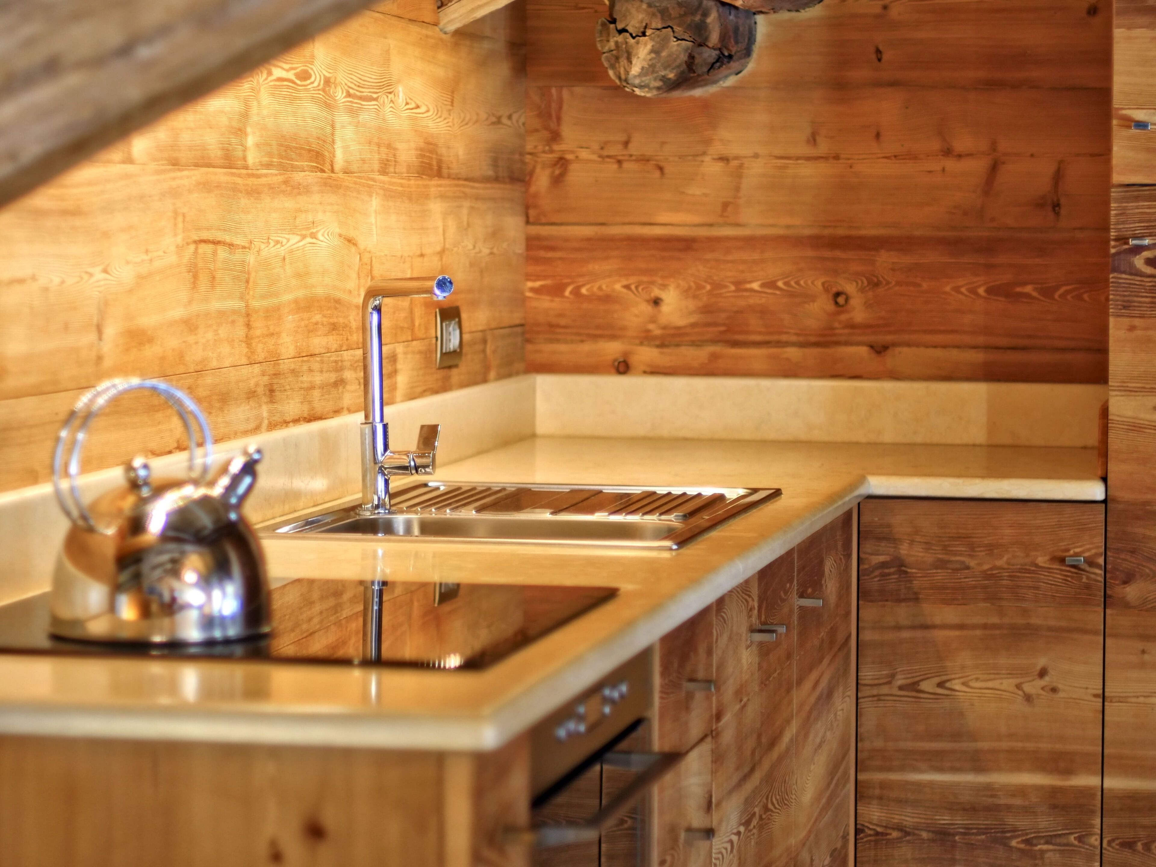 A modern kitchen with wooden cabinetry, a stainless steel sink, and a kettle on the countertop.