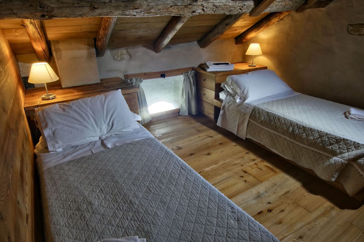 A cozy attic bedroom with two beds, wooden beams, and a rustic aesthetic.