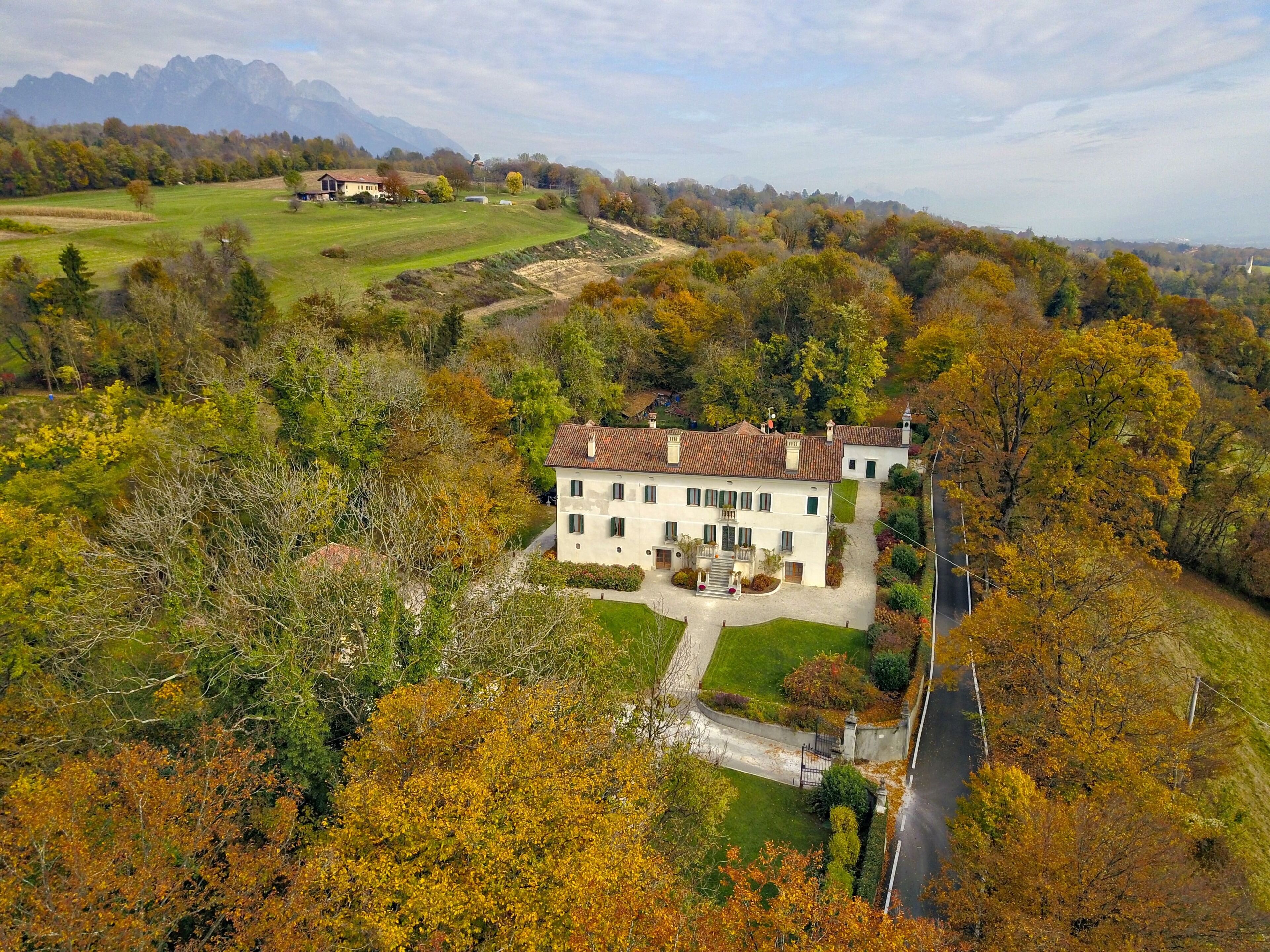 A large, two-story house with a tiled roof, surrounded by a well-maintained lawn and trees with autumn foliage.
