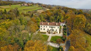 A large, two-story house with a tiled roof, surrounded by a well-maintained lawn and trees with autumn foliage.