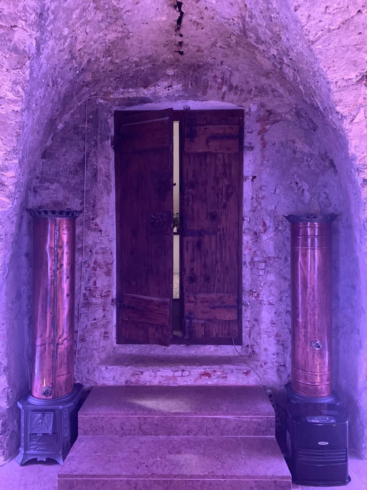 An arched doorway with a wooden door, flanked by two cylindrical objects on either side.