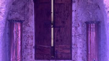 An arched doorway with a wooden door, flanked by two cylindrical objects on either side.
