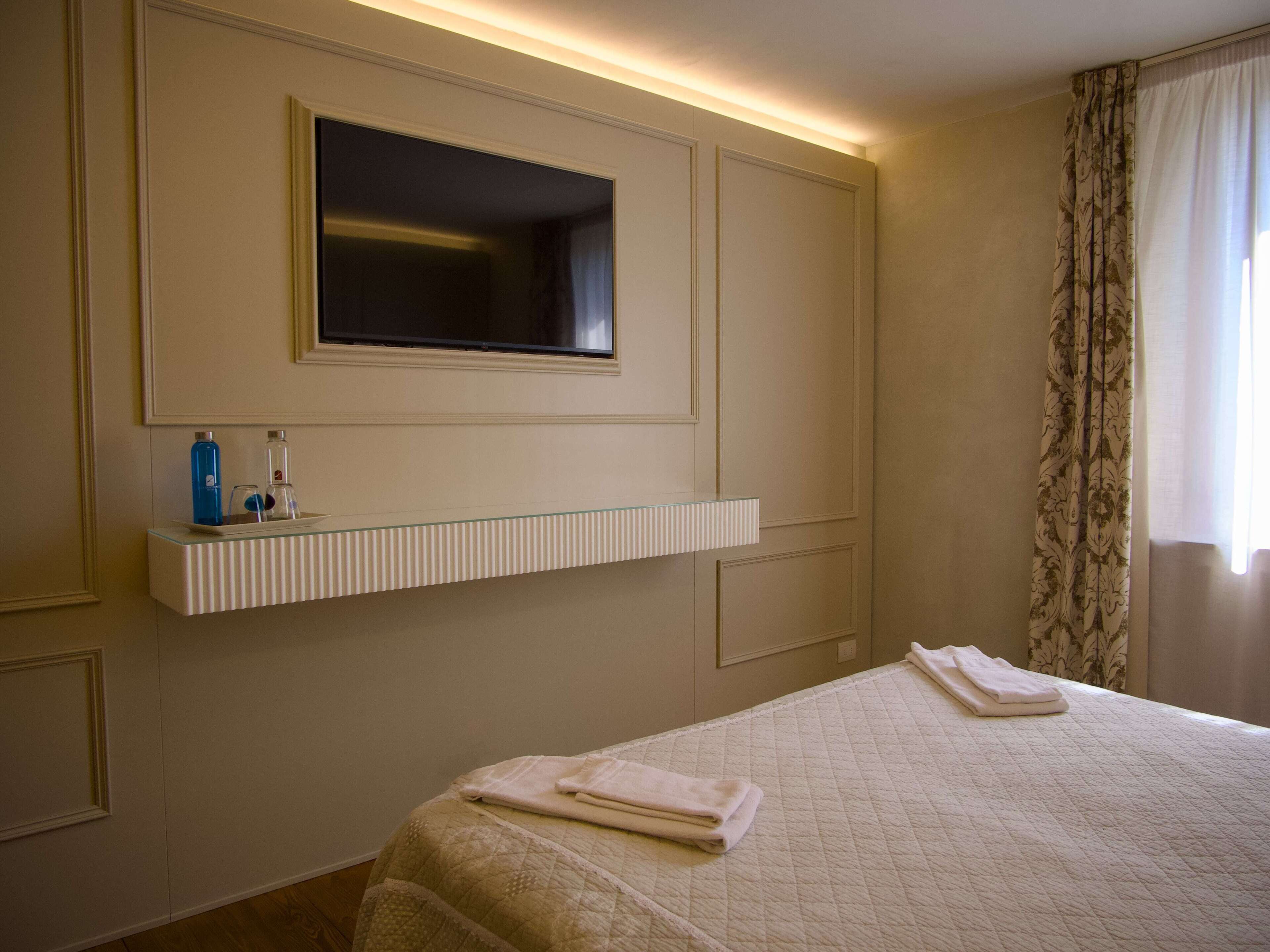 Una camera d'albergo con un letto, un comodino con articoli da toilette, uno specchio e una finestra con tende.