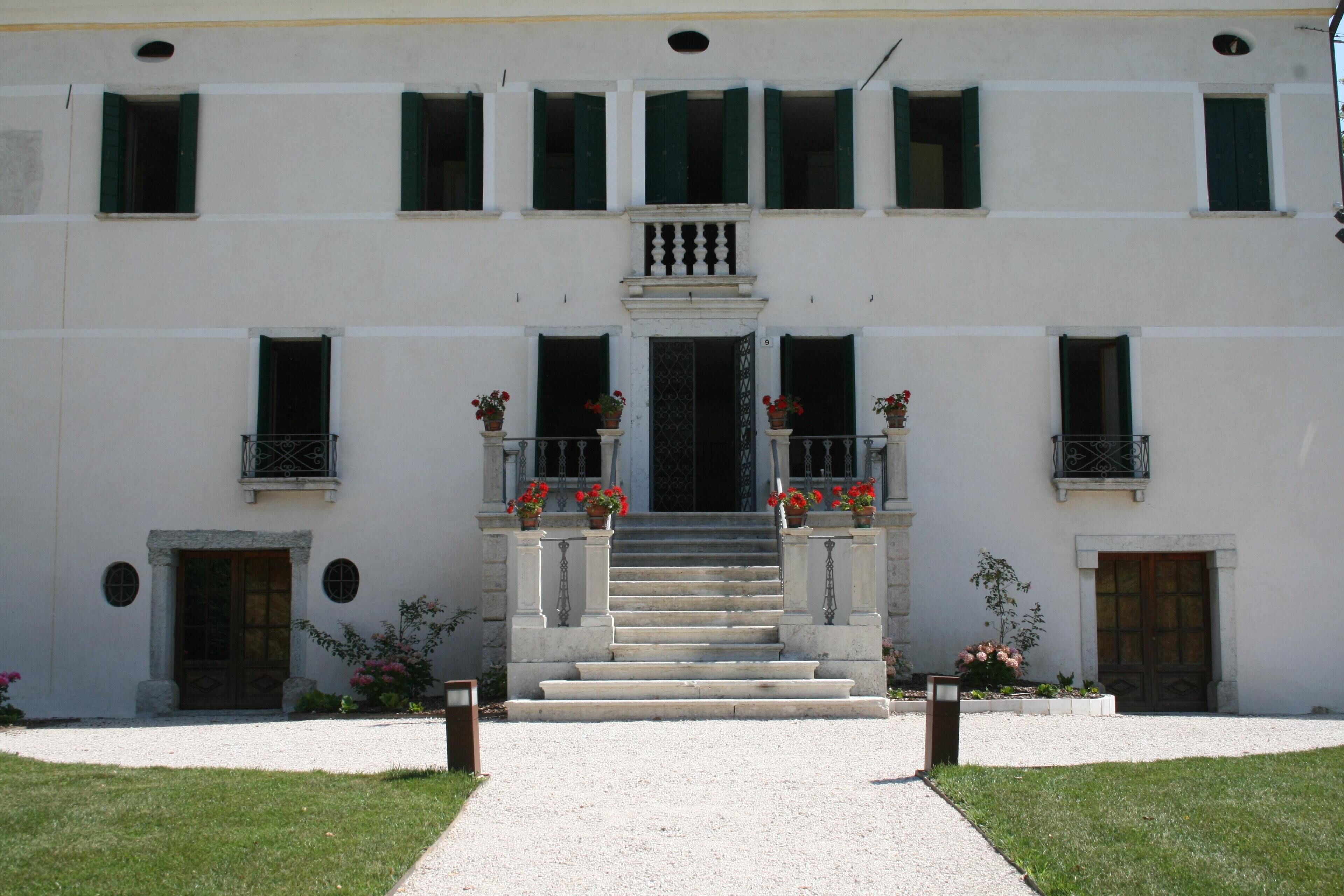 A building with a symmetrical facade, a central entrance with steps, and multiple windows with green shutters.