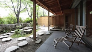 Un espace extérieur aménagé, abrité et doté de sièges, avec des marches en pierre menant à une terrasse en bois, le tout entouré de verdure.