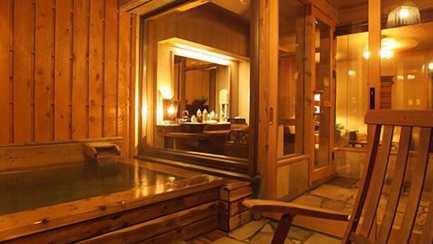 Un intérieur en bois avec un jacuzzi, un fauteuil et un miroir qui reflète une pièce dotée d’une cheminée.
