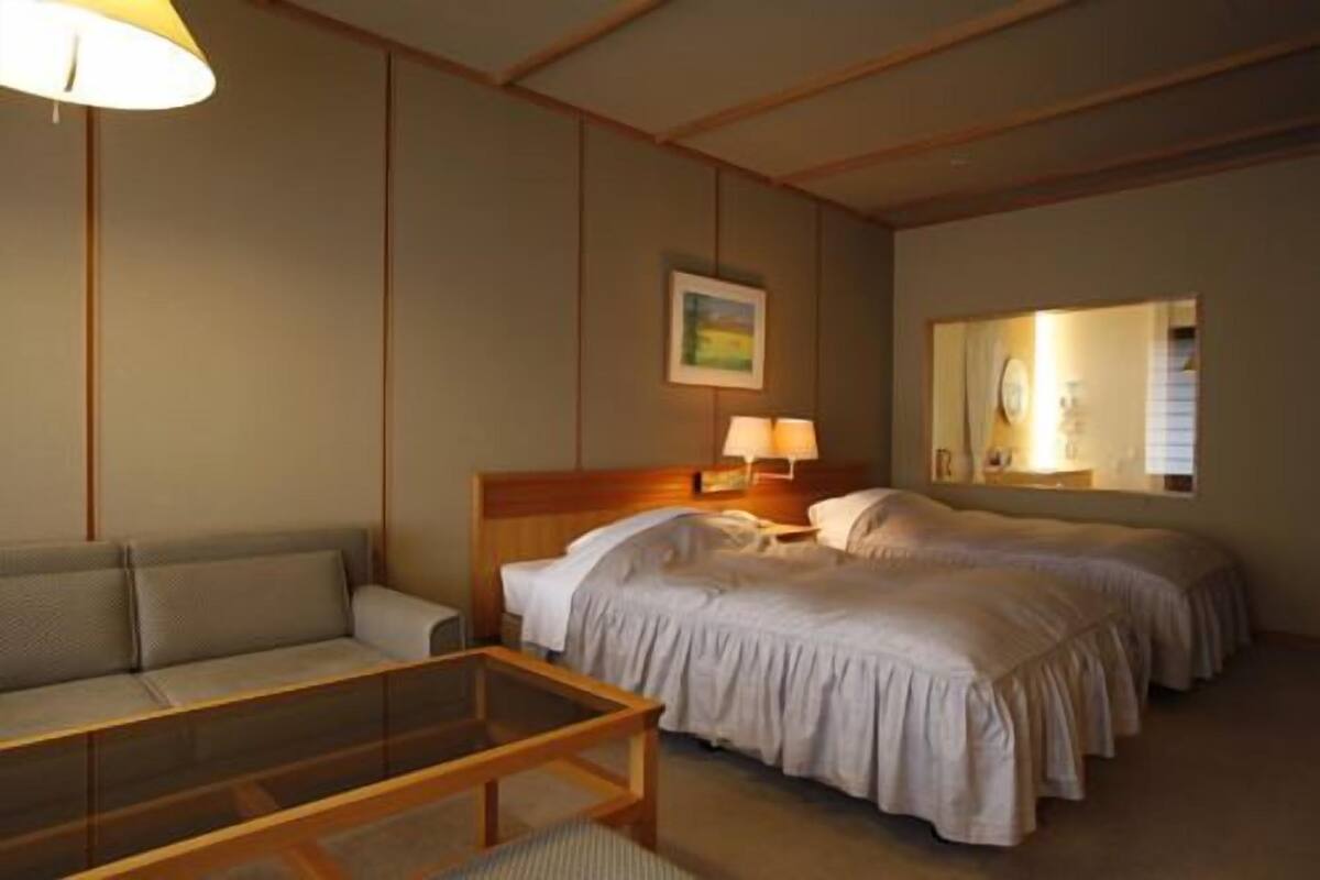 A hotel room with two beds, a sofa, a glass coffee table, and a painting on the wall.