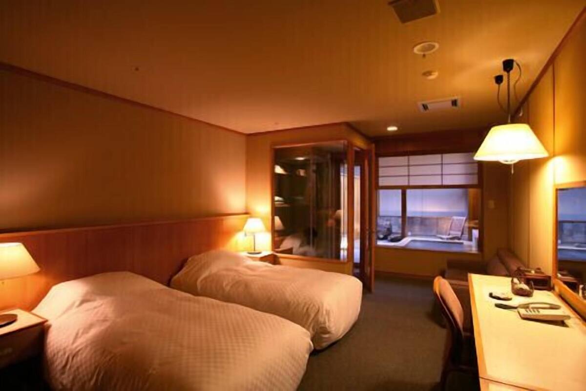 A hotel room with two beds, a desk, and a window with a view.