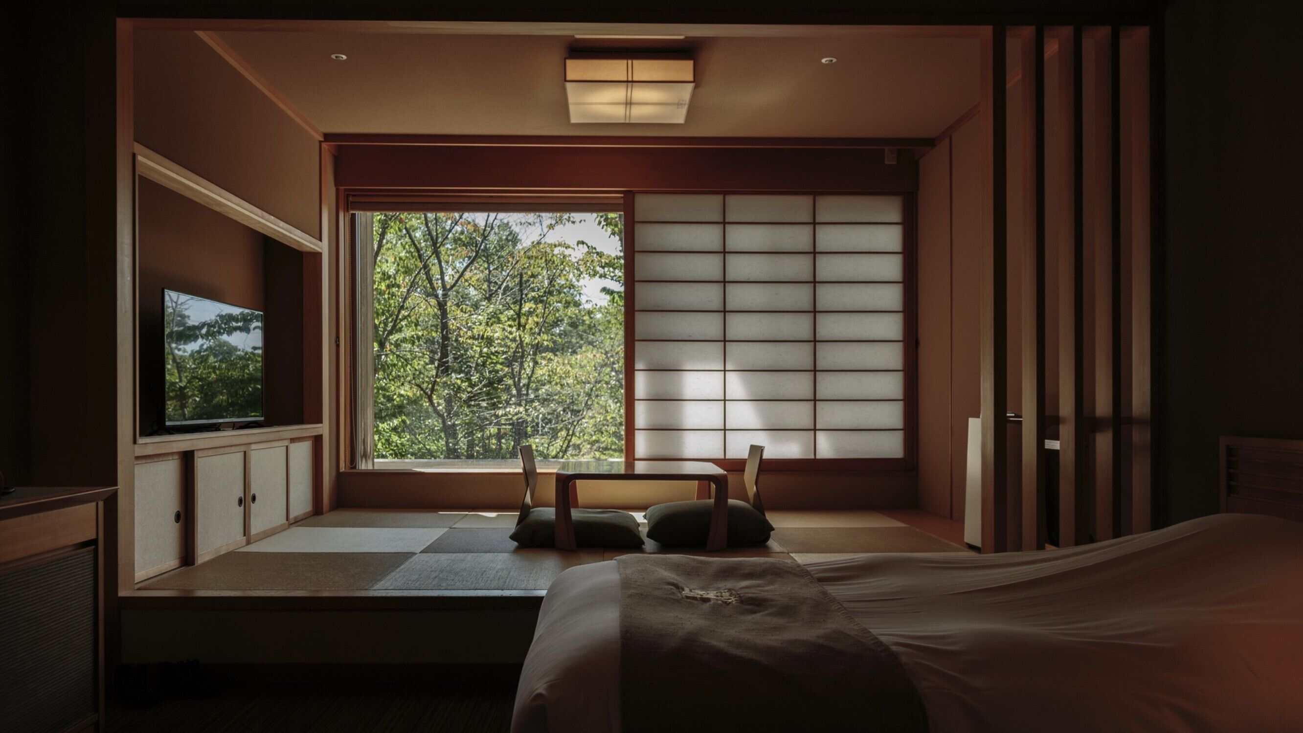 A traditional Japanese-style room with tatami flooring, a low bed, a television, and a sliding shoji screen.