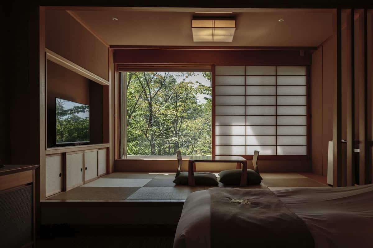 A traditional Japanese-style room with tatami flooring, a low bed, a television, and a sliding shoji screen.