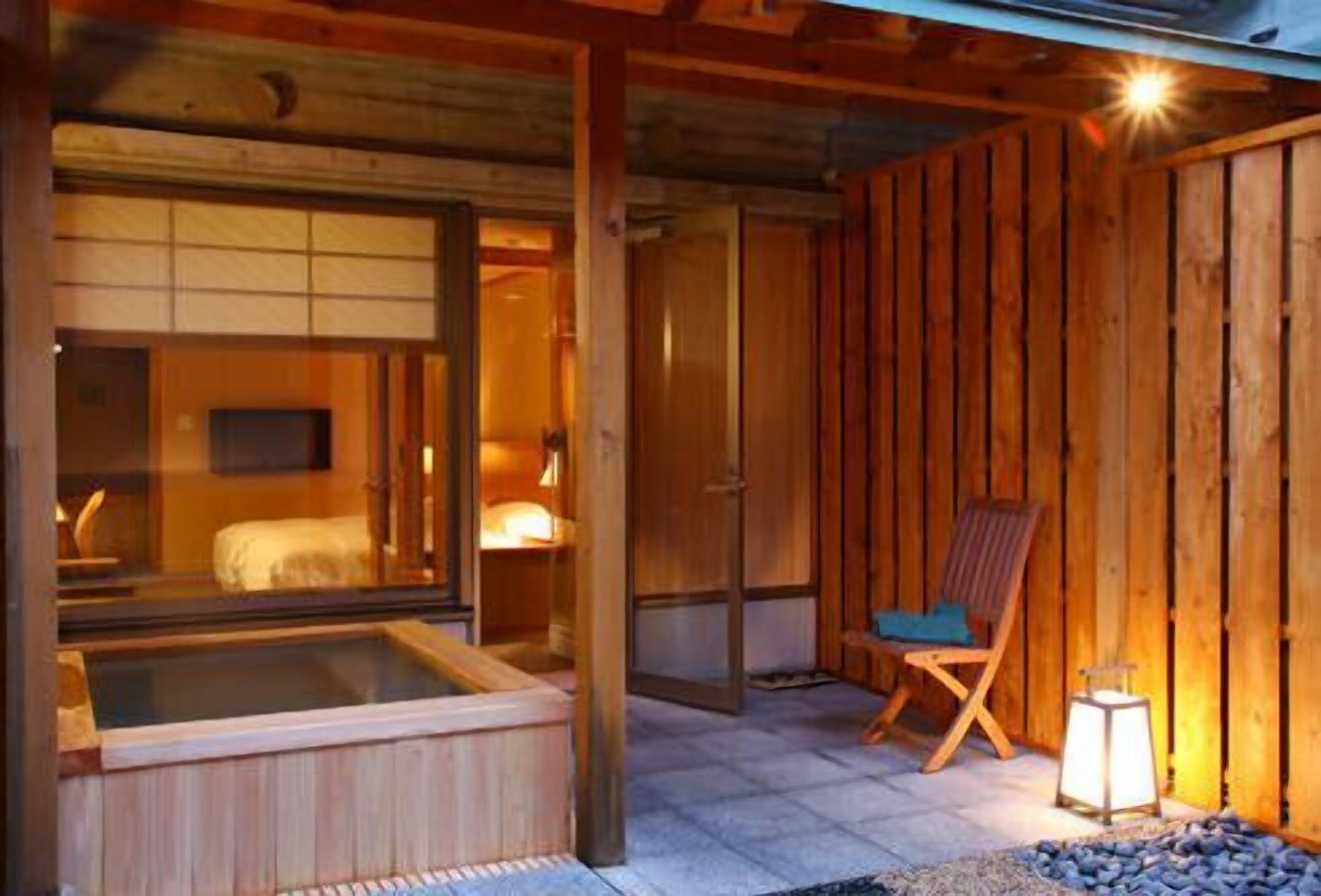 A traditional Japanese-style room with a wooden interior, a hot tub, and a chair by a lantern.