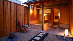 Une façade en bois, un espace extérieur aménagé avec des sièges couverts, un chemin en pierre et une pièce visible avec une baignoire.