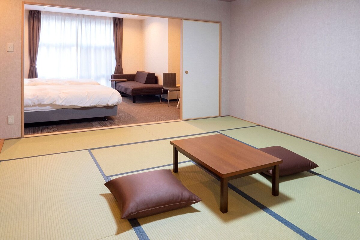 Ein Hotelzimmer mit Tatami-Böden, einem Bett, einer Couch, einem Tisch und einem Spiegel.