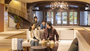 A group of people sitting on a sofa in a lobby with a staircase and a chandelier. - Ooedo Onsen Monogatari Premium Enakyo (Ena)