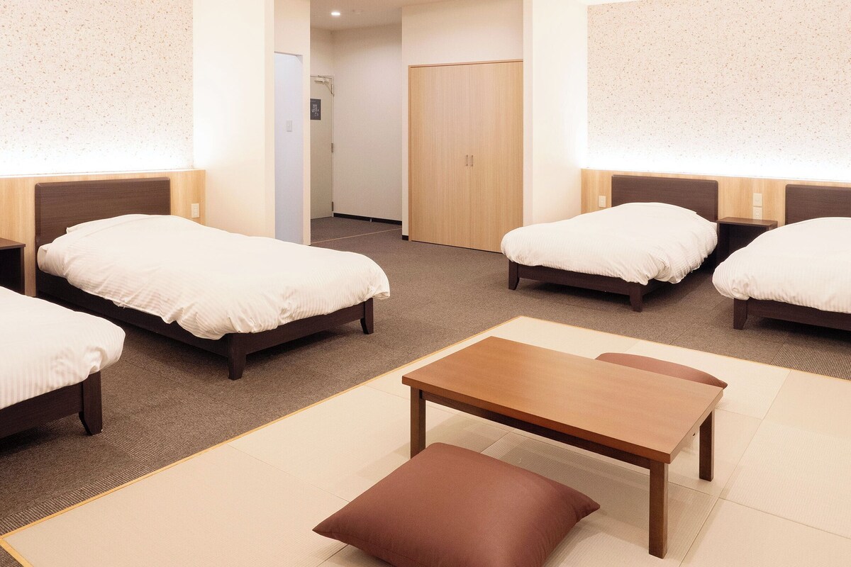 Ein Hotelzimmer mit vier Einzelbetten, einem Holztisch und einem braunen Kissen.